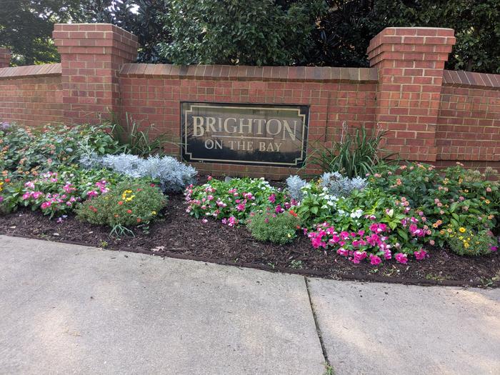 The Brighton on the Bay neighborhood entrance sign, framed by brick columns and flowering shrubs
